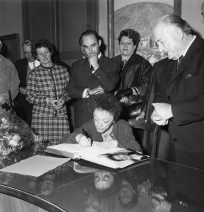 Edith Piaf signe le livre d'or de la ville. Derrière elle, Guy Henras et le maire à droite